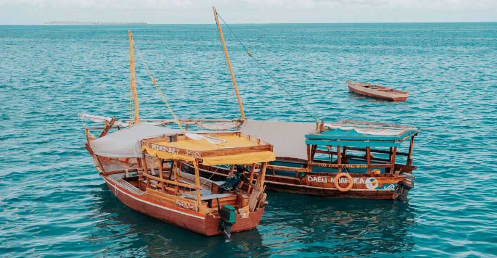 Aerial or shoreline view of Zanzibar turquoise water, white sand and traditional dhows at sunset